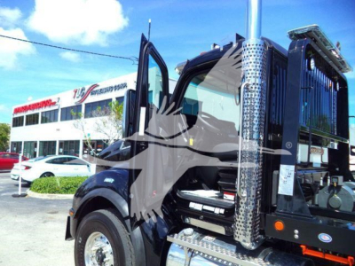 Kenworth T880 rollback truck cab with open doors showing chrome vertical exhaust and steps, dealership lot in background.