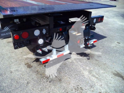 Rear view of a flatbed trailer hitch on a Kenworth T880 rollback truck showing tail lights, hydraulic hoses, and reflective red/white safety stripes.