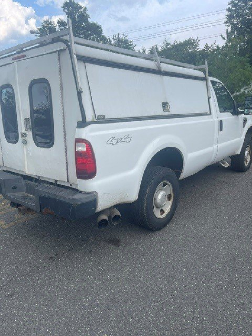 Ford F-250 Super Duty pickup with utility cap viewed from rear-left side showing 4x4 badge and dual exhaust, white body, in-service condition.