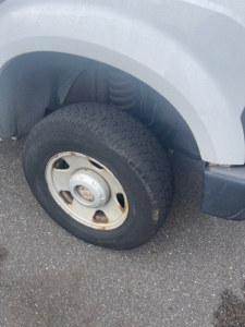 Front left wheel and fender of a Ford Super Duty F-250 SRW; wheel with steel rim, tire, suspension components visible.