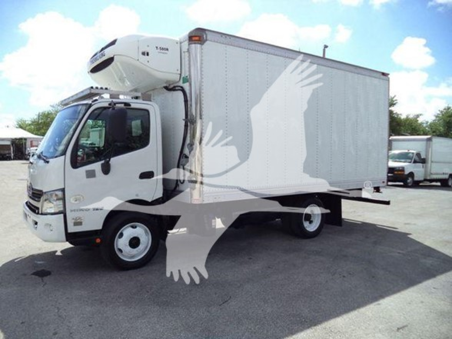 Truck with refrigerated box and rooftop refrigeration unit, white cab, side view showing JHHHDM2H7KK004004 VIN and stock number T04004 on listing.