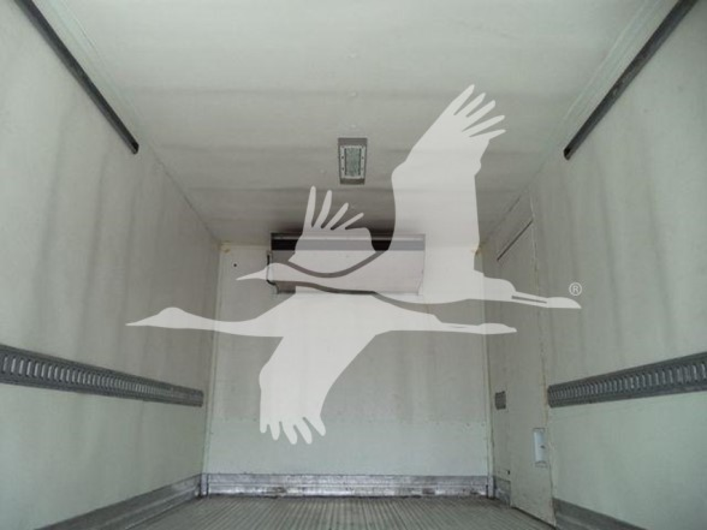 Inside a refrigerated truck cargo area with blank walls and ceiling; overhead vent; small ceiling light.