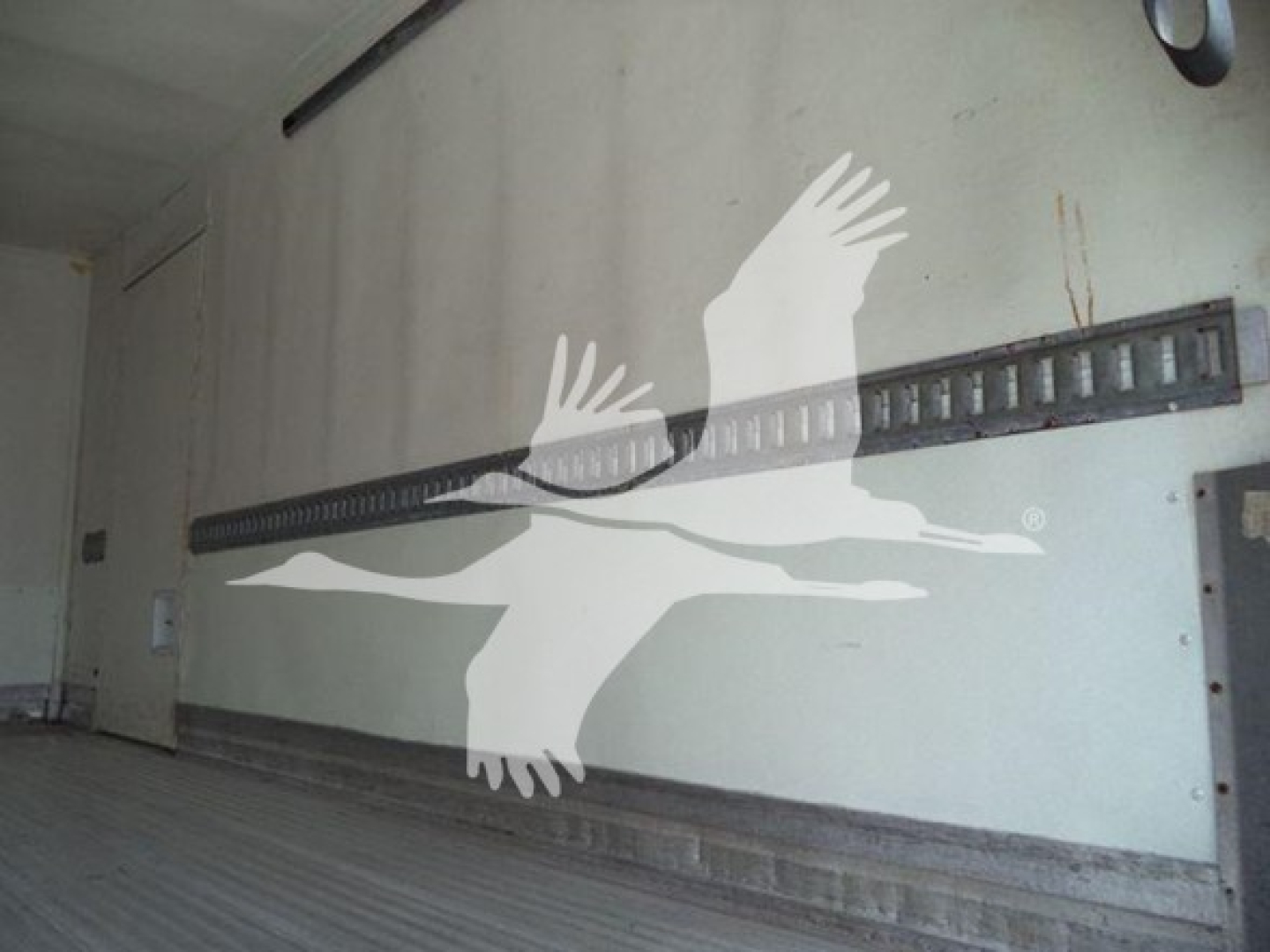 Interior wall of a refrigerated truck with a horizontal double-rail track and some faint text on the wall
