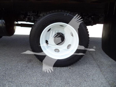 Wheel and tire under a refrigerated truck trailer showing white steel wheel and black tire.