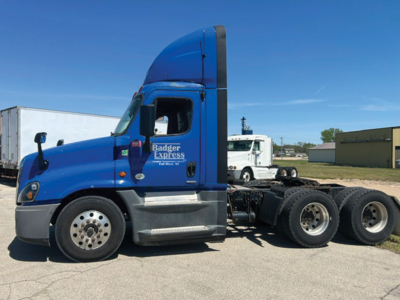 Truck side view showing blue 2015 Freightliner Cascadia125 Evolution tractor with driver door text and multiple rear axles.