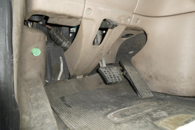Cab floor area of a Freightliner Cascadia 125 daycab showing pedals and driver-side footwell with rubber floor mat and underlying wiring.