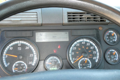 Dashboard view of a Freightliner Cascadia 125 cab with multiple gauges including tachometer, speedometer, and warning lights; faint digital display shows 85°F and various indicators.