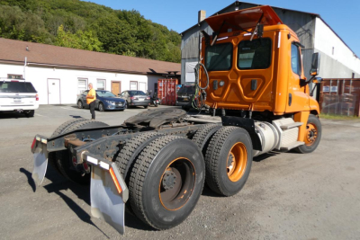 Freightliner Cascadia 125 daycab tractor rear view showing chassis and wheels with orange cab and black tires.