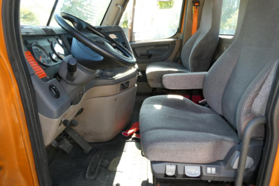 Cab interior of a Freightliner Cascadia 125 truck showing driver seat, steering wheel, and passenger seat with gray upholstery.