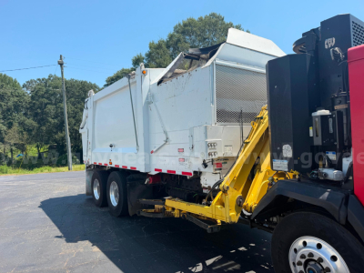 Truck-mounted crane loader showing garbage truck body in white with yellow crane arm attached to a red cab, triple rear axles, stock number and category not visible on image