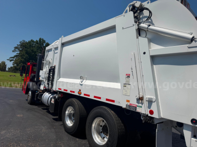 Truck-mounted crane carrier dump body showing side view with dual rear wheels and hydraulic hydraulic components on the right, white with red reflective stripe.