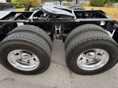 Dual rear tractor axles of a Kenworth truck chassis with chrome wheels and dual tires, showing suspension and fifth wheel area.