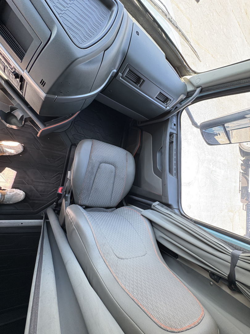 Truck cab interior view from driver's side showing gray fabric seats with orange piping, dashboard, and door area of a Volvo VNL cabin.