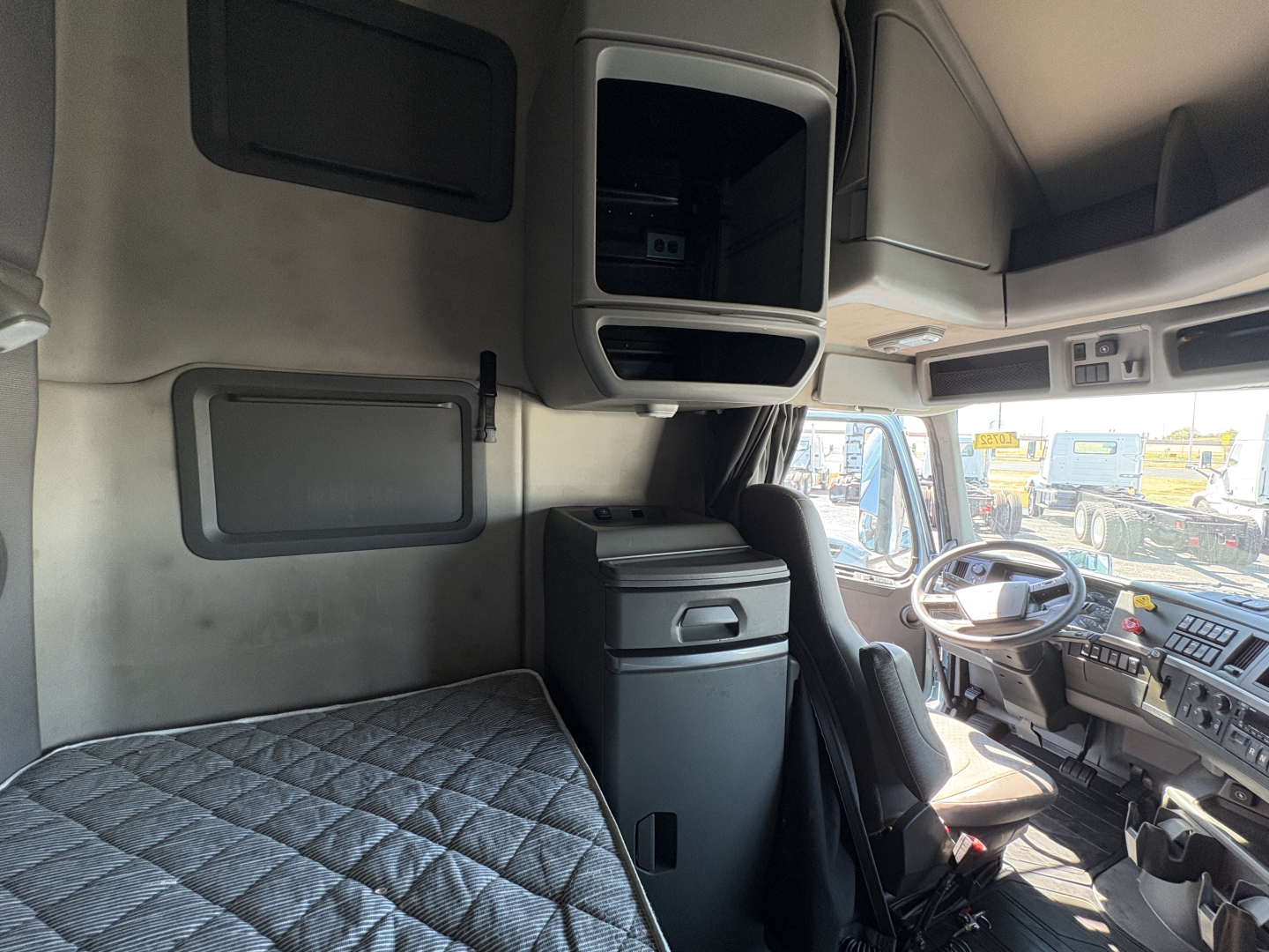 Truck cab interior of a Volvo VNL64T760 showing sleeper area with storage compartments and driver seat; dashboard and window visible.