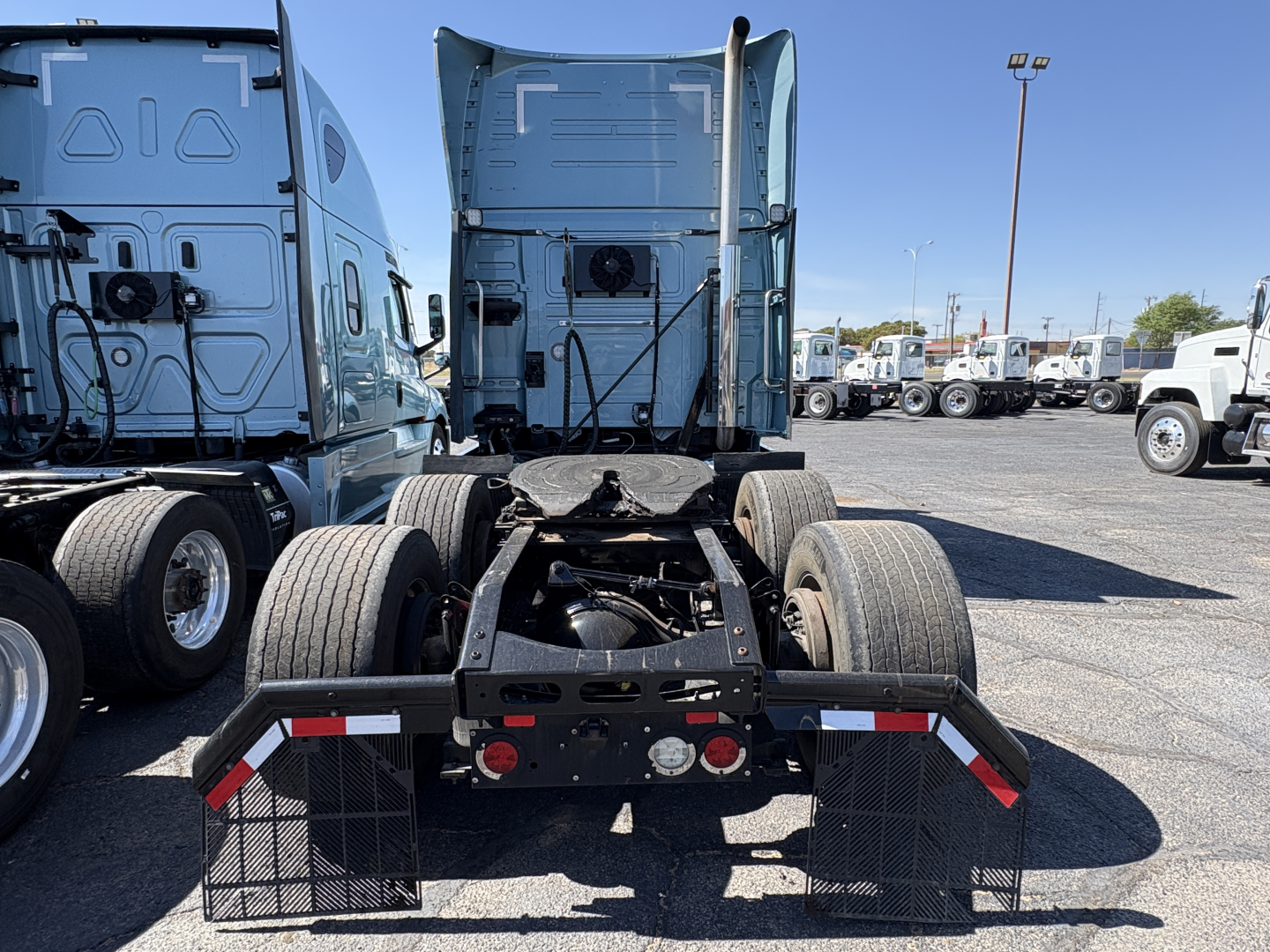 Truck chassis rear view showing fifth-wheel coupling and dual rear axles of a 2022 Volvo VNL64T760 Sleeper tractor with surrounding trucks in a lot.