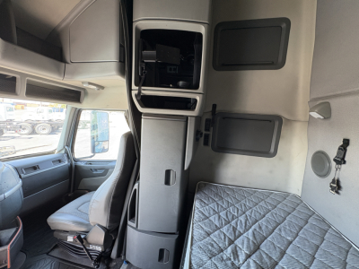 Interior of a Volvo VNL truck cab showing sleeper area with quilted bed cover and storage compartments, pilot seat visible, center console, and dashboard edge.