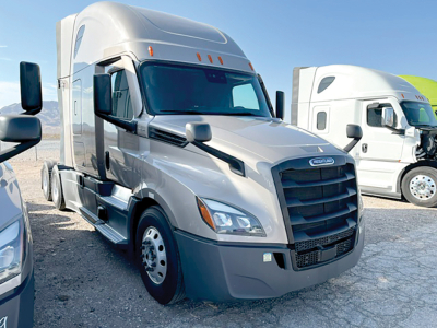 Truck front view in a dealership lot: 2024 Freightliner Cascadia126 with gray cab, black grille, aerodynamic mirrors, and sleeper cab.