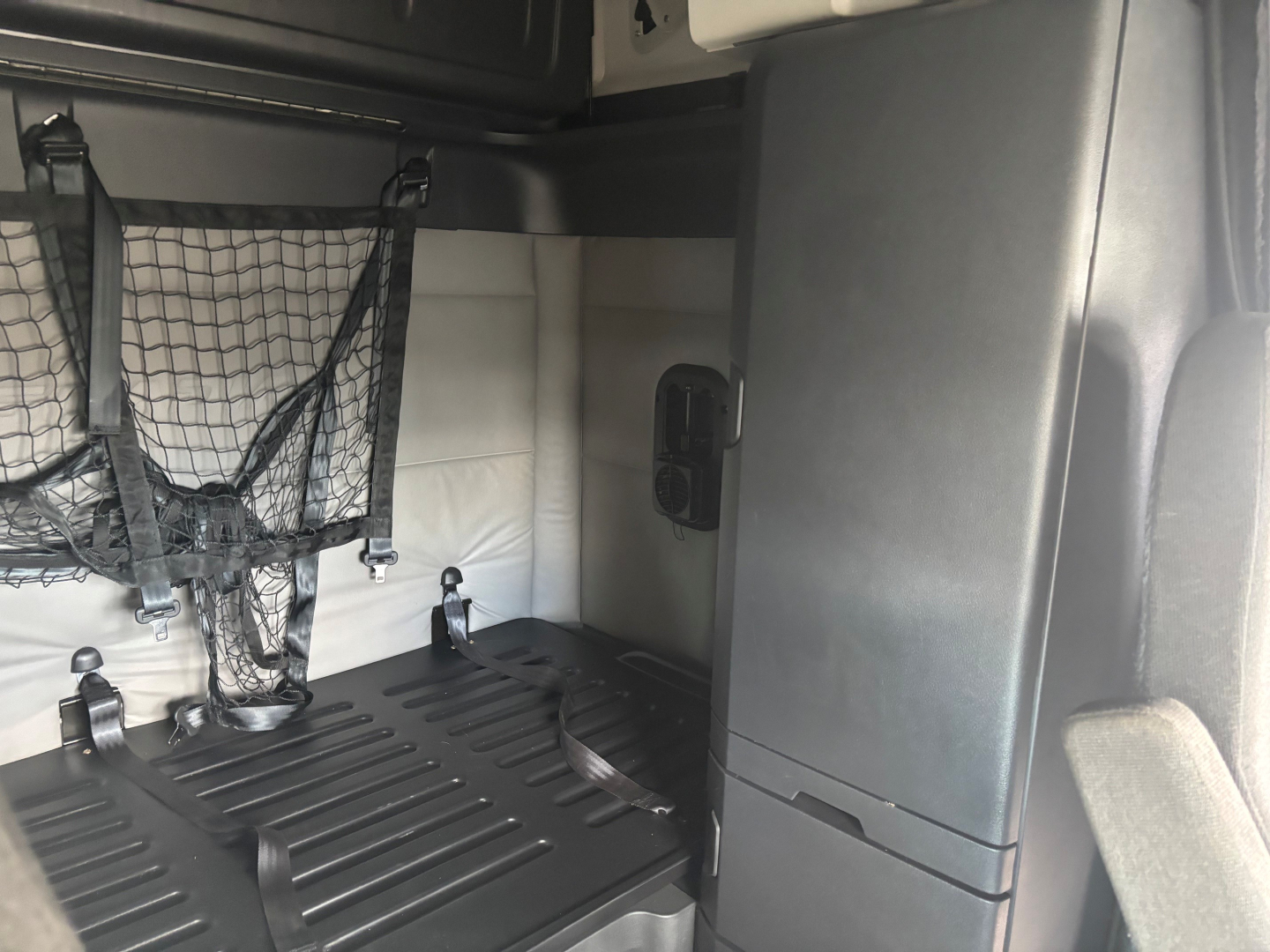 Truck cab interior cargo area with netted storage, vertical grey panel, and black ridged floor in a Freightliner CA-126 sleeper, view from passenger side.