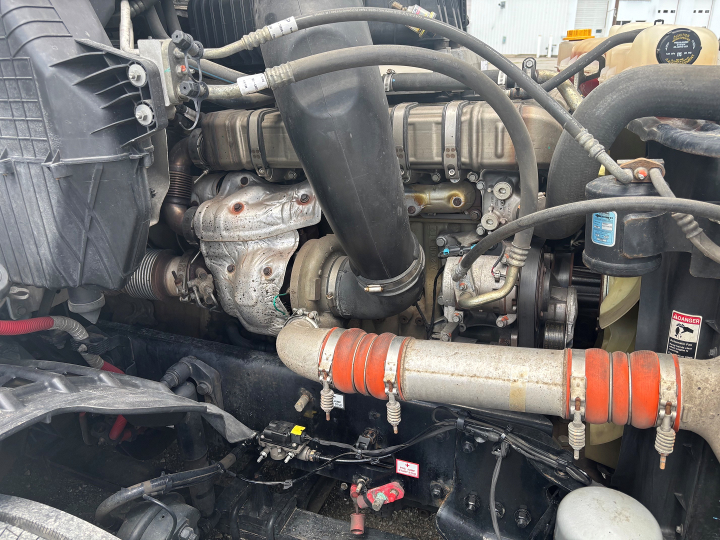 Engine bay of a Freightliner CA-126 with visible turbocharger, hoses, intake, and orange silicone intercooler hose clamp; VIN label and components partially obscured.
