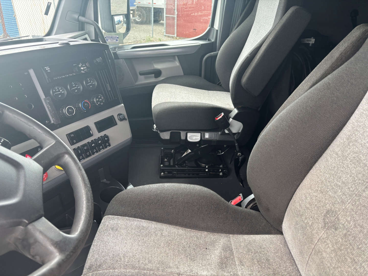 Truck interior showing driver and passenger seats, dashboard with control panel, steering wheel, and center console.