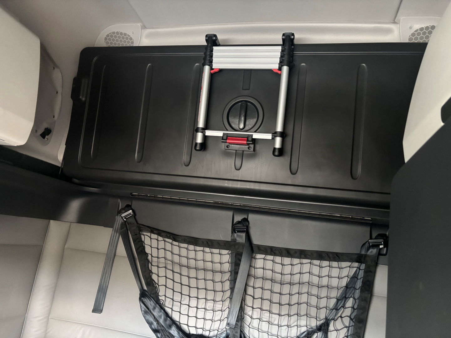 Cargo area of a 2021 Freightliner CA-126 sleeper truck showing storage area and netting with a folded floor ladder device.