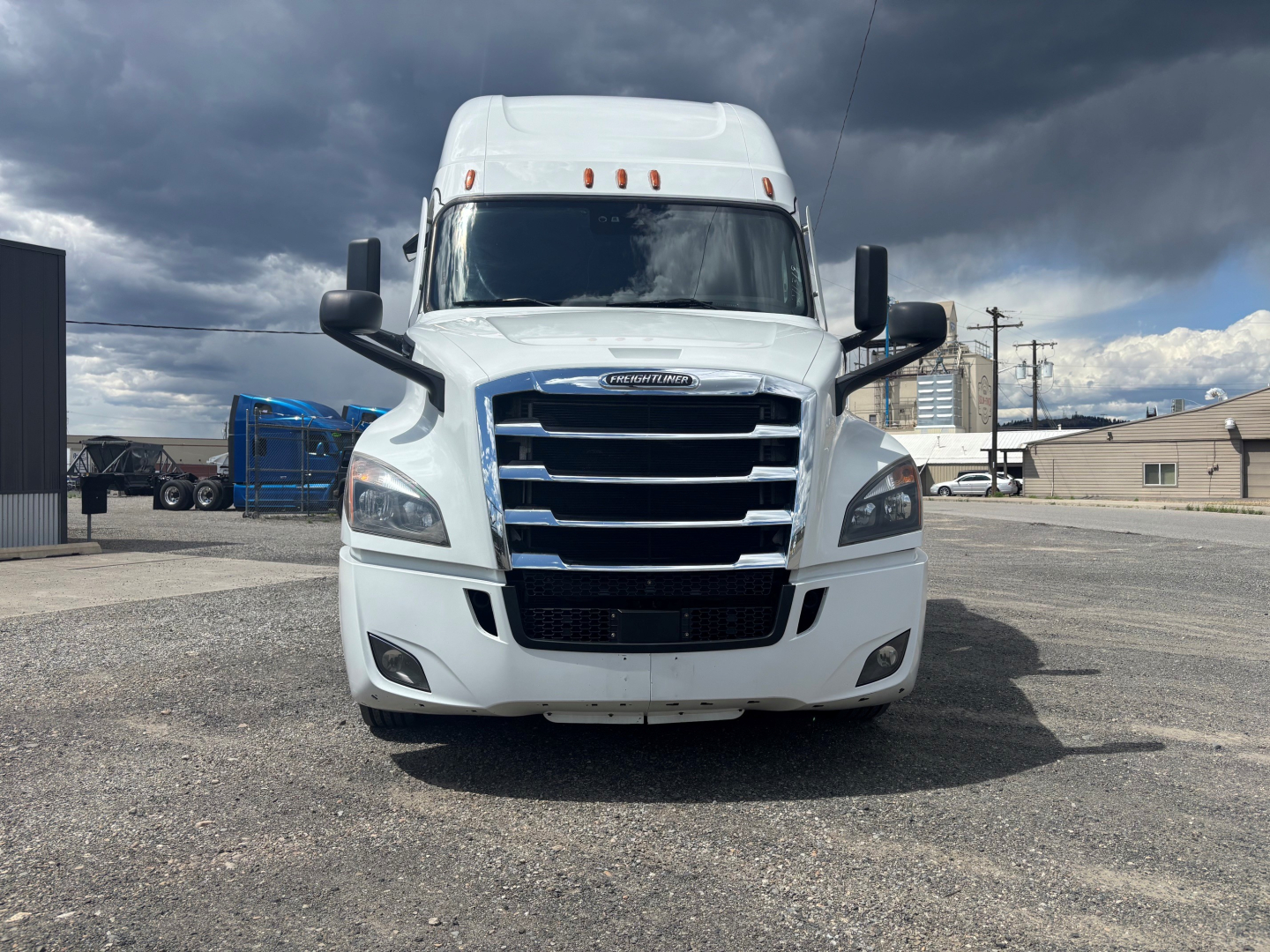 Front view of a white Freightliner cab with large grille and bumper, twin large mirrors, and top sleeper hood. Headlights visible.