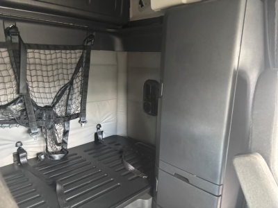 Truck cab interior cargo area with netted storage, vertical grey panel, and black ridged floor in a Freightliner CA-126 sleeper, view from passenger side.