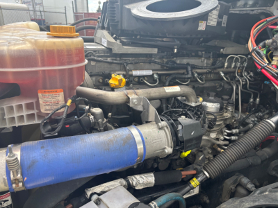 Engine bay of a Freightliner CA-126 showing blue intercooler piping, yellow dipstick, red coolant reservoir, and various hoses and wiring harnesses.