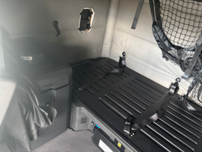 Freightliner CA-126 sleeper cab interior cargo area with storage box and straps; visible labels on black ribbed deck and a net on the right side.
