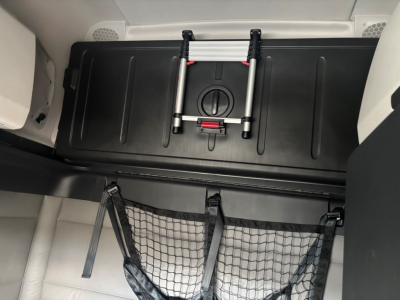 Cargo area of a 2021 Freightliner CA-126 sleeper truck showing storage area and netting with a folded floor ladder device.