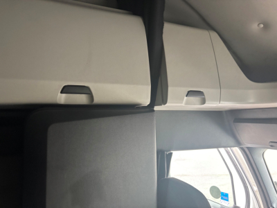 Cab interior showing overhead storage compartments and part of windshield, with light gray panels.