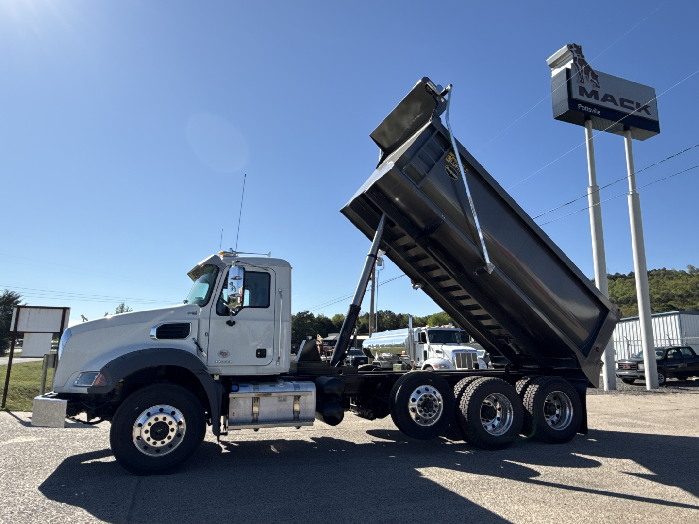 Dump truck in raised bed configuration showing Mack GR84B truck and wheel set along with VIN plate area and stock number at a dealership.