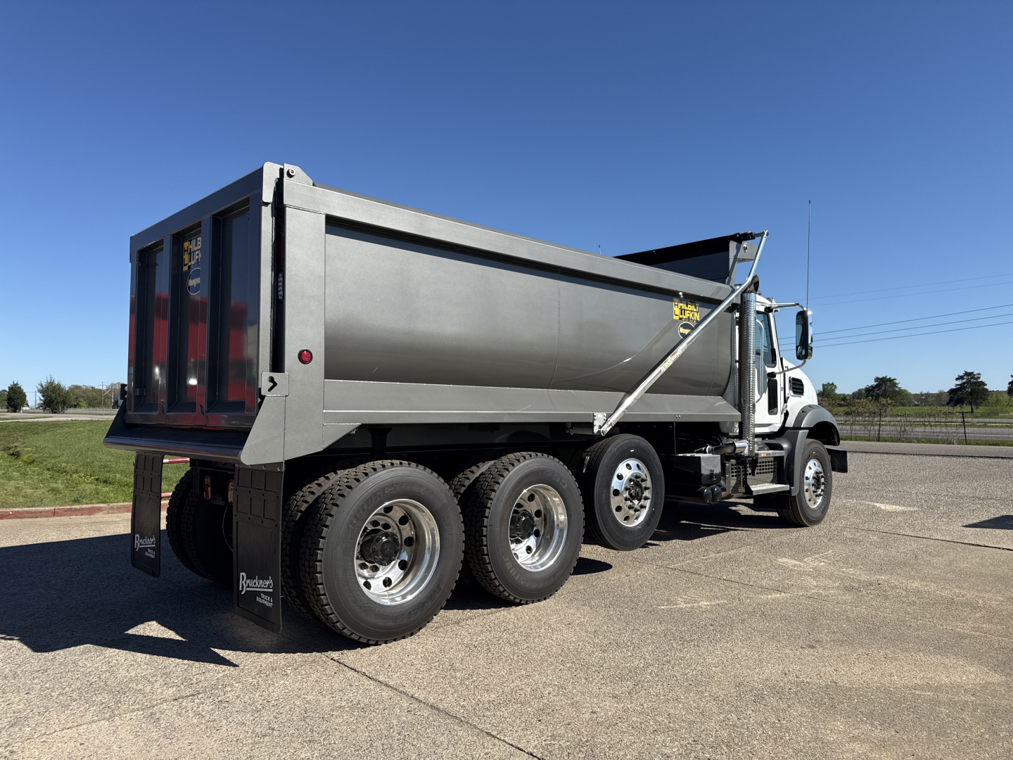 Dump truck side view showing large gray dump bed on a Mack GR84B chassis with triple rear axles and dual wheels, VIN tag not visible