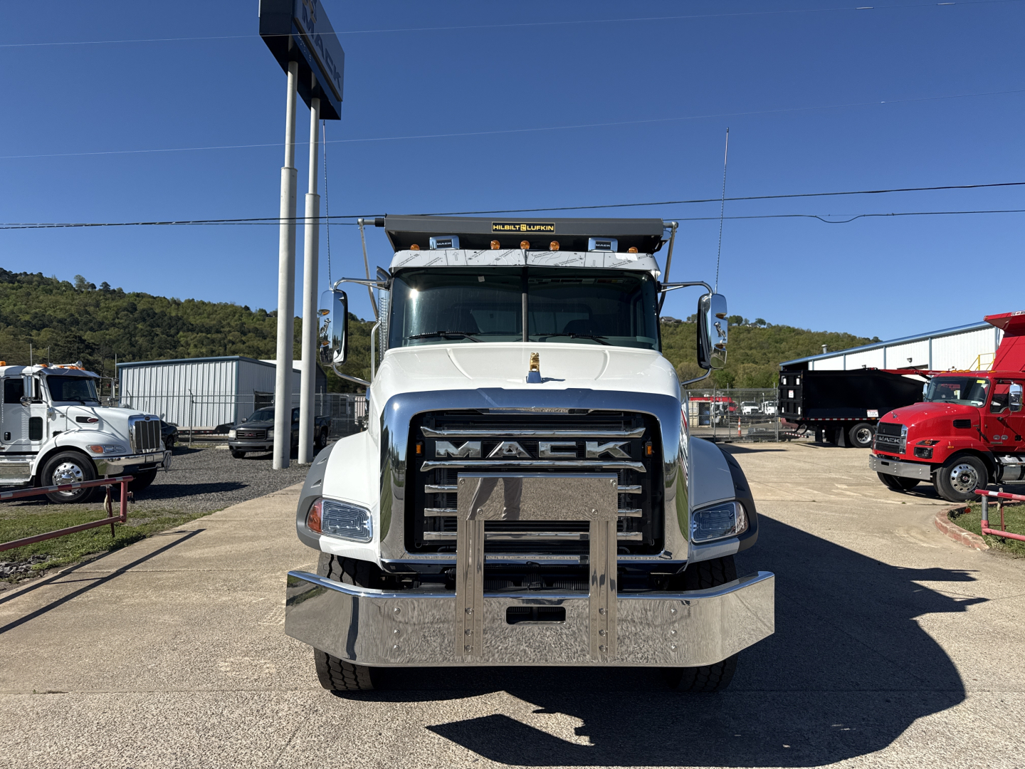 Front view of a white 2026 Mack GR84B dump truck showing large grille with Mack emblem and chrome bumper; clear windshield with side mirrors; construction setting.