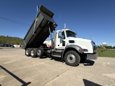 Dump truck with raised dump bed on a white Mack GR84B with three-axle configuration, front cab chrome bumper, side view showing vehicle details.