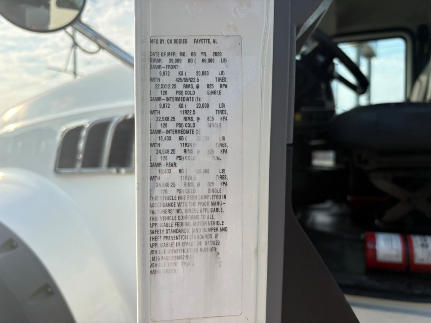 Vehicle information sticker on the door jamb of a Mack truck showing specs and numbers in small print.