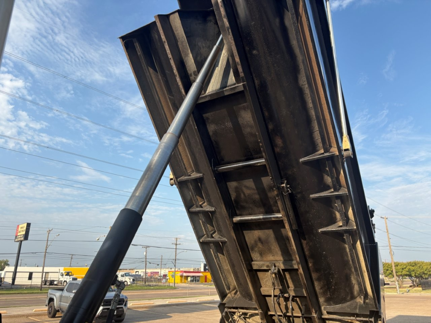 Truck dump bed raised with hydraulic cylinder visible, metal frame and underside details.