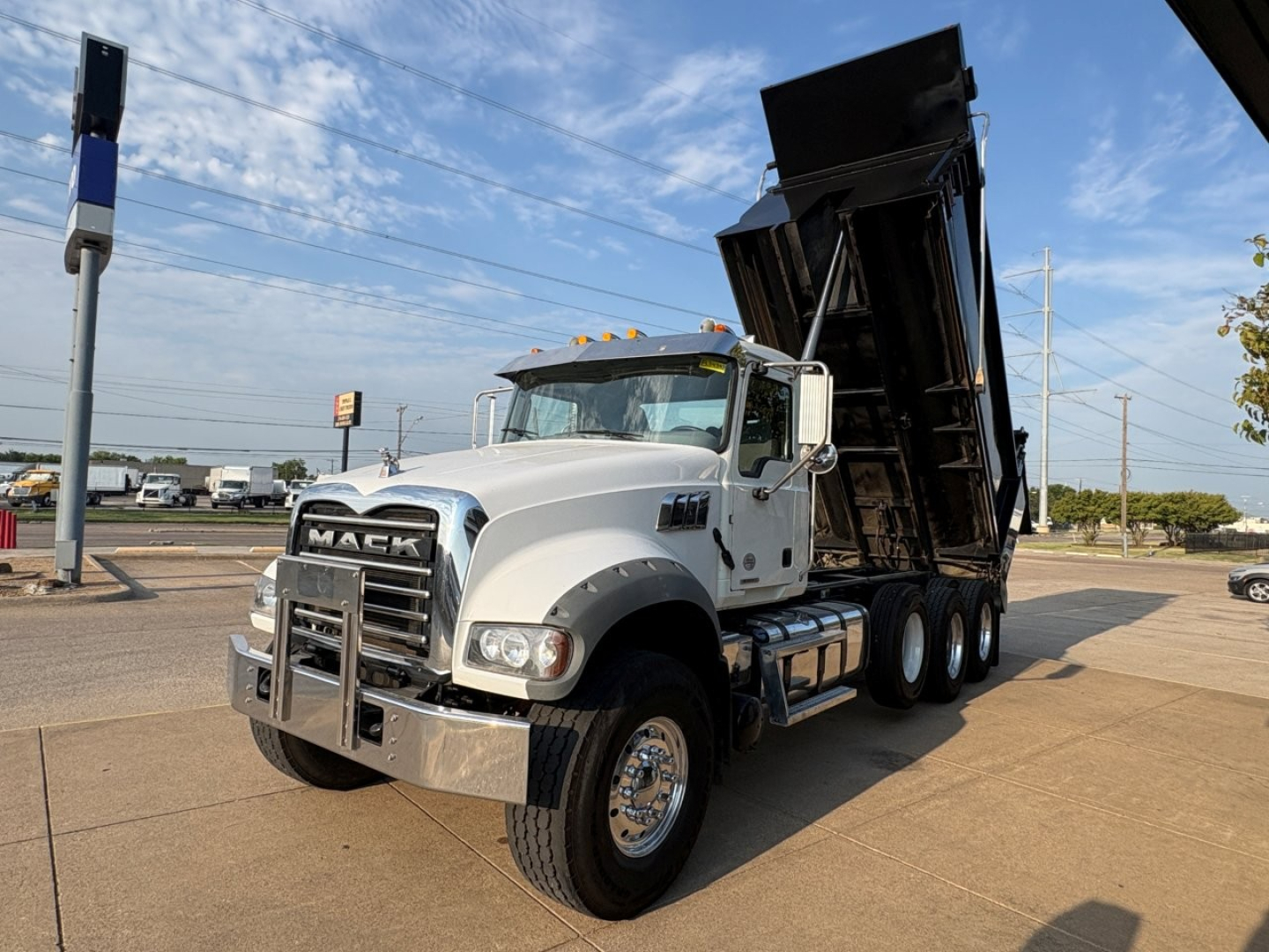 Mack GR64F dump truck with raised dump bed in a dealership lot.