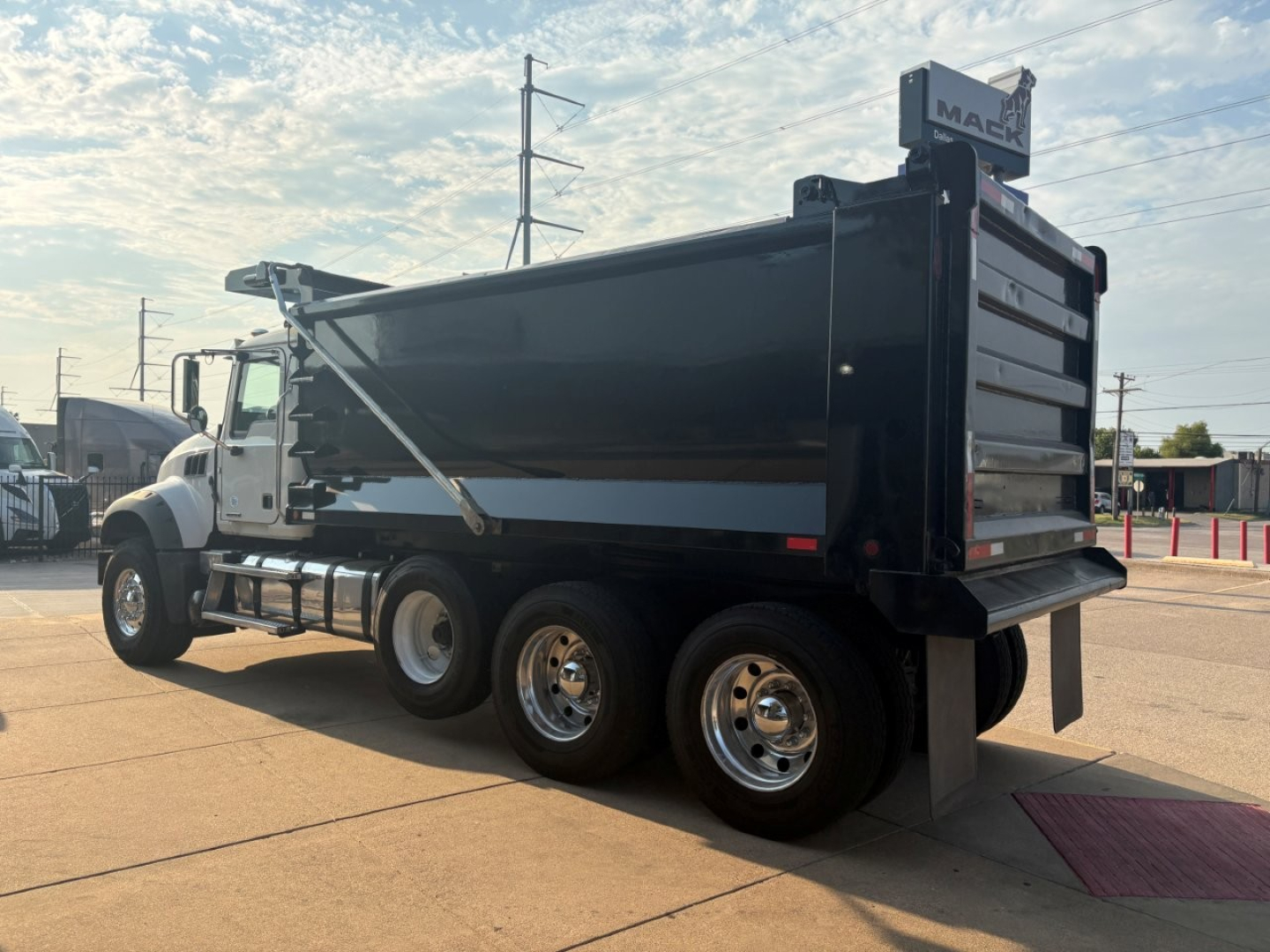 Dump truck showing side view of a black Mack GR64F dump bed with chrome wheels and rear tailgate. Visible text includes MACK on the cab and high-mounted sign, plus reflective striping on the side.