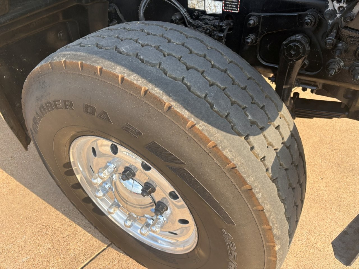 Tire and dual-wheel front hub on a Mack GR64F dump truck showing treaded tire and polished chrome valve area with lug nuts.