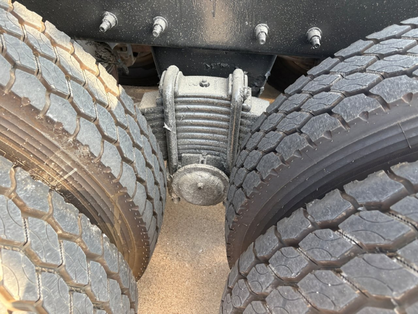 Mack GR64F truck rear view showing drivetrain linkage and dual rear tires; close-up of suspension hub and leaf spring assembly between tires.