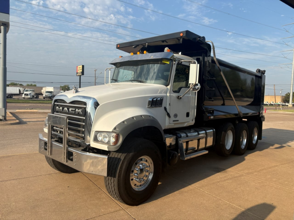 Mack GR64F dump truck in side-front view with white cab and black dump body, chrome bumper, dual rear axles, and raised dump bed.