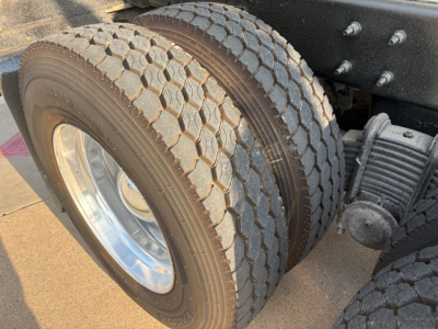 Front dual rear axle tires of a dump truck showing dual tires and part of suspension; visible tread pattern and wheel rims.