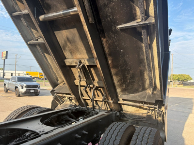 Mack GR64F dump truck bed raised showing underside and dual rear wheels, hydraulic cylinders, and metal chassis.