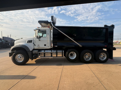2021 Mack GR64F dump truck side view showing large black dump bed, white cab, three rear axles, chrome wheels, and hydraulic mechanism.