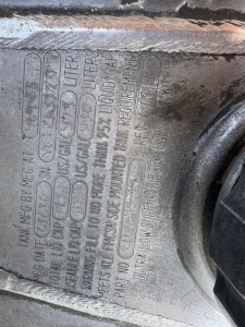 Mack GR64F engine bay label showing fluid capacities and warnings embossed in metal; includes text blocks such as 'DIESEL FUEL', 'LIQUIDS', and capacity lines near a cap.