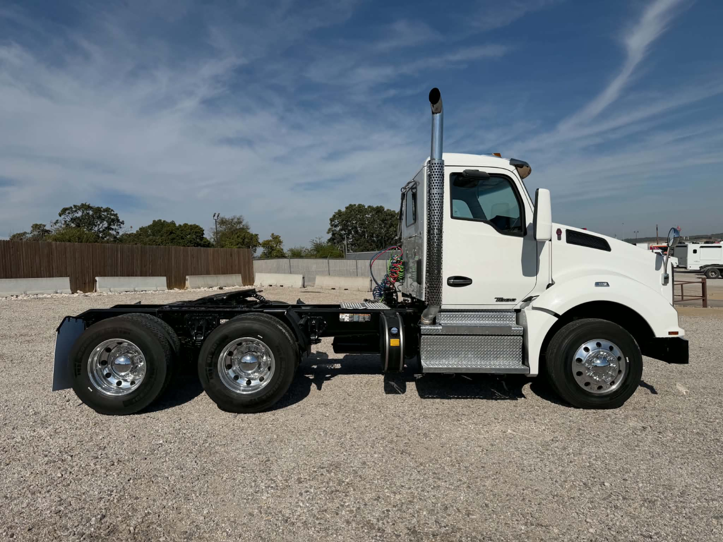 Kenworth T880 conventional daycab truck side view showing white cab, dual rear axles, chrome fuel tanks, exhaust stack, and bare chassis.