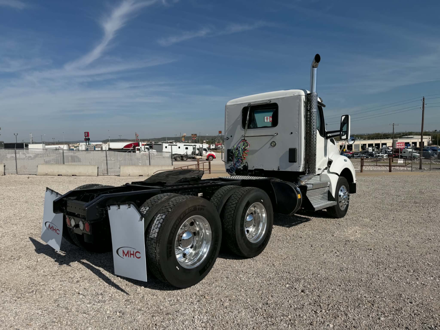 Kenworth T880 tractor tractor rear view showing dual rear axles and chrome wheels, white cab, exhaust stack, and mud flaps.