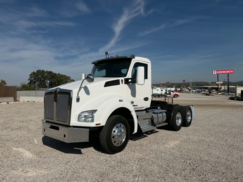 Kenworth T880 truck cab showing front windshield, side mirror, and white heavy-duty truck in a gravel lot.