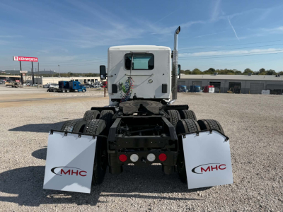 Kenworth T880 rear view showing mud flaps with MHC logos, fifth wheel, and dual rear axles in a gravel lot.